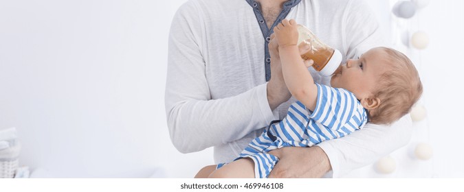 Father holding his baby, giving him drink from a bottle, panorama