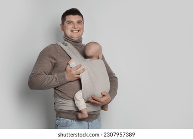 Father holding his child in sling (baby carrier) on light grey background. Space for text - Powered by Shutterstock