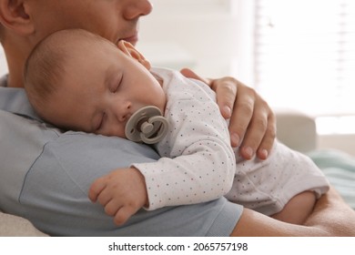 Father holding his cute sleeping baby with pacifier at home, closeup