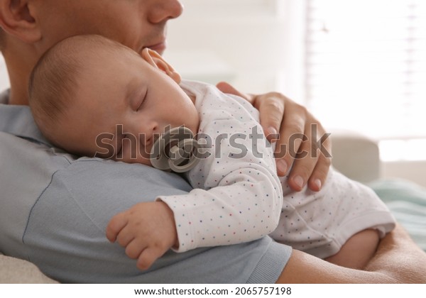 Father holding his cute sleeping baby with\
pacifier at home,\
closeup