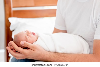 Father Holding In His Hands Sleeping Newborn Baby Daughter. Parent Dad Sitting In The Bed With Napping Infant Child At Home