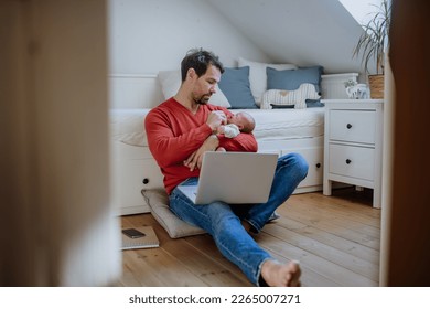Father holding his newborn crying baby during working on laptop.