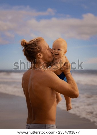 Father holding, kissing his infant baby boy son high in the air on sandy beach. Family travel and summer vacations concept. Family outdoor activities. Seminyak beach, Bali, Indonesia