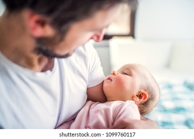 Father holding a sleeping toddler girl at home.