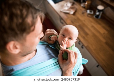 Father holding small baby, carrying him around house in baby carrier. Unconditional paternal love, father's Day. - Powered by Shutterstock