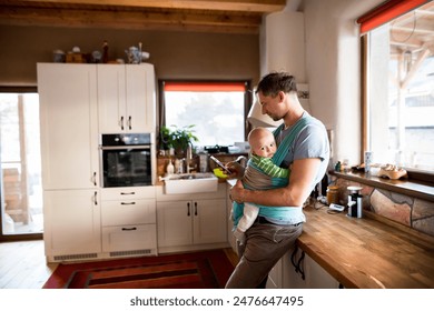 Father holding small baby n baby carrier, standing in kitchen scrolling on smartphone. Unconditional paternal love, father's Day. - Powered by Shutterstock