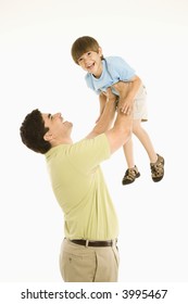 Father holding smiling son up overhead against white background.