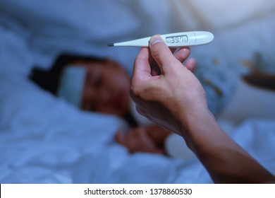 Father Holding Thermometer Foreground Of Sick Little Girl In Bedroom At Night Time For Monitor High Fever With Thermometer For ,Kid Had High Fever And Tepid Sponging To Bring The Temperature Down