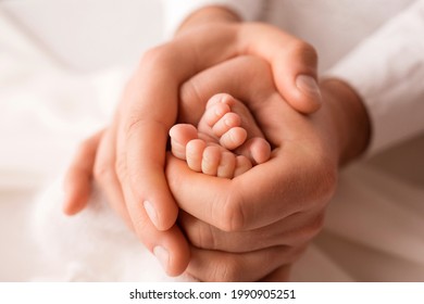 The father holds the bare feet of the newborn on a white background. Tiny legs in the hands of a man. Family, parents and homework concept. Health care, pediatrics. 