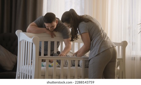 Father holds daughter or son in his arms and gives baby to wife. Loving mother puts baby in bodysuit in crib. Parents plays with newborn baby arms and legs. Concept of childhood, parenthood and family - Powered by Shutterstock