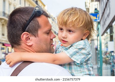 Father holds a tired child in his arms while walking around the city. Dad calming down his son  hugging him. Family walking.