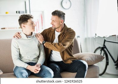 Father Hugging Teen Son On Sofa At Home