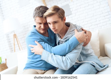 Father Hugs Son While Sitting With Him At Home On The Couch. Father And Son Forged Family Relationships Together.