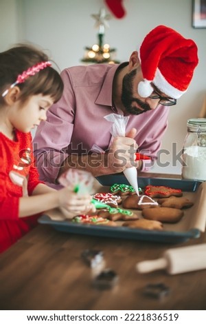 Father ib Santa Claus hat and his little daughter decorating gingerbread Christmas cookies