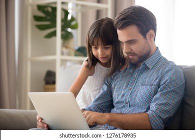 Father And Kid Girl Using Laptop At Home Looking At Screen Choosing Goods Online, Happy Dad Talking To Child Daughter Showing New Computer Application Watching Video, Doing Internet Shopping Together