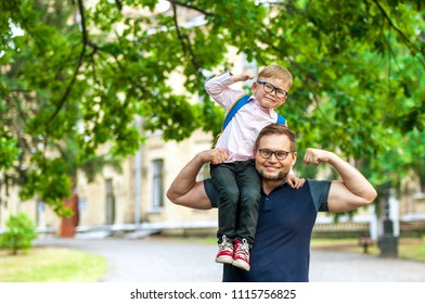 Father And Kid Have Fun - Child On Dad's Shoulders. Parent Taking Child To School. Back To School. Superman Dad And Son Having Fun. Concept Of Friendly Family.