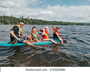 Father with kids swimming on paddle surf board on lake river. Dad with children doing sport recreation seasonal summer water activity. Sporty family friends. 