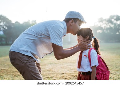 father kiss her daughter forehead when taking her to school in the morning. primary student first day