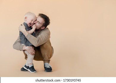 Father Kissing His Baby Son On Beige Studio Background. Laughing And Hugging Family. Father's Day