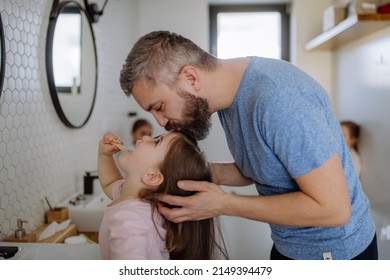 Father kissing his daughter while she is brushing her teeth in bathroom, morning routine concept. - Powered by Shutterstock