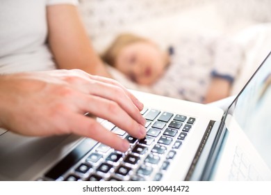 Father with laptop and a sleeping toddler boy in bed at home.