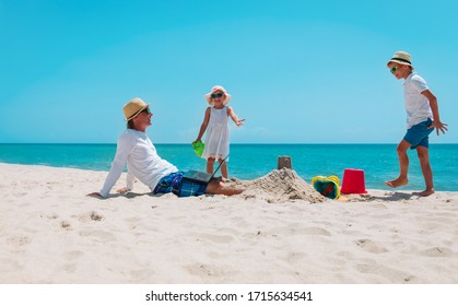 Father With Laptop Trying To Work And Kids Play With Sand On Beach