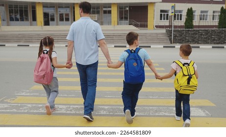 father leads child school holding his hand. dad takes children across road by hand. pedestrian crossing school building. happy family concept. children zebra crossing. parent leads boy girl sister. - Powered by Shutterstock