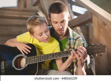 father learning his boy to play guitar, they sit on the steps of a country house on a warm summer evening. - Powered by Shutterstock