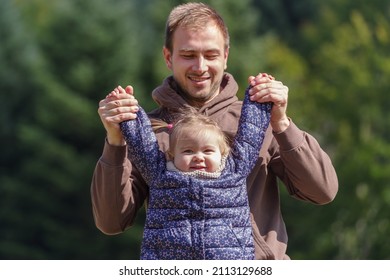 Father Lifting A Cheerful Toddler Daughter Outdoors In Nature