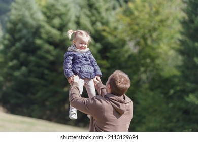 Father Lifting A Cheerful Toddler Daughter Outdoors In Nature