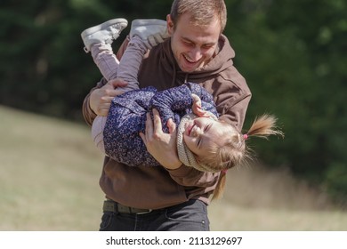 Father Lifting A Cheerful Toddler Daughter Outdoors In Nature