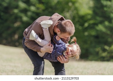 Father Lifting A Cheerful Toddler Daughter Outdoors In Nature