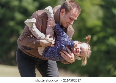 Father Lifting A Cheerful Toddler Daughter Outdoors In Nature