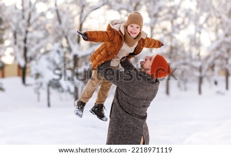 Father lifting little son up while having fun together outdoor on frosty day, happy dad and kid playing in winter park, enjoying snowy weather, actively spending New year holidays on fresh air