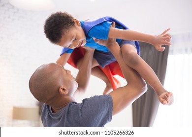 Father lifting son up with super hero costume at home