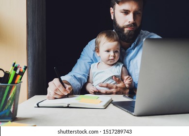 Father with little baby on knees making notes in notebook, looking at laptop. Young man holding child and working on PC. Parent sitting home and getting distant education. Dad doing homebased business