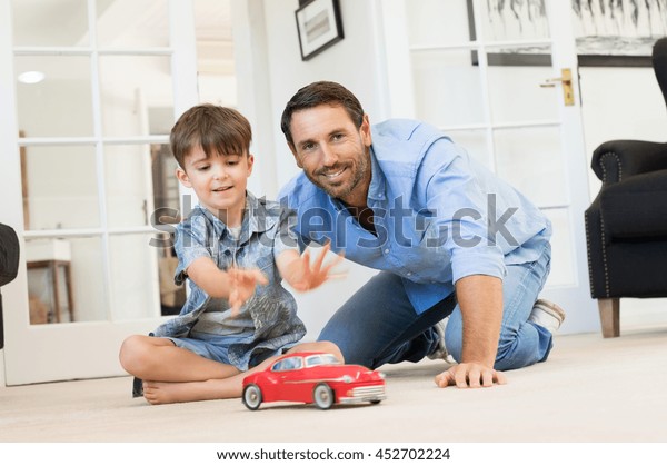 Father with little boy playing with toy car.\
Smiling father and happy son playing together in living room.\
Father spending quality time with son at\
home.