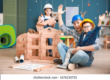 Father And Little Children Dressed As Builders Playing With Take-apart House At Home