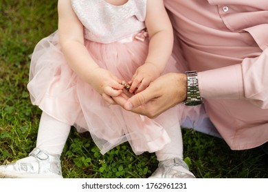 Father And Little Daughter Playing On Grass. Baby Girl In Cute Dress Holding Her Dad's Hand. 