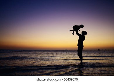 Father and little daughter silhouettes on beach at sunset