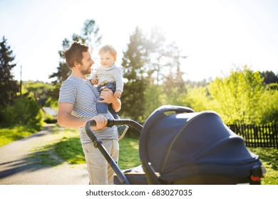 Father with little son and baby daughter in stroller. Sunny park