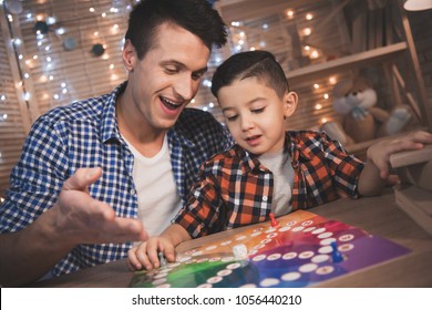 Father And Little Son Are Playing Board Game At Table At Night At Home.