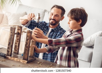 Father and little son together at home standing at table boy helping dad hammering nail into chair leg smiling joyful cooperation - Shutterstock ID 1281507340