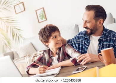 Father and little son together at home sitting at table dad praising boy for good grades smiling proud cheerful while doing homework