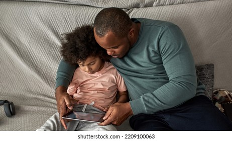 Father And Little Son Using Digital Tablet On Sofa At Home. Young Black Family Lifestyle And Relationship. Leisure And Entertainment. Fatherhood And Parenting. Man And Child Spending Time Together