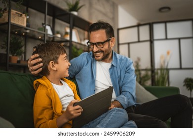 Father look son while he play video games or browse internet on tablet and enjoy at home - Powered by Shutterstock