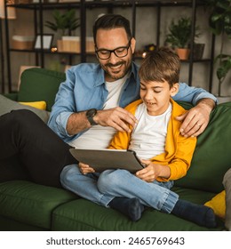 Father look son while he play video games or browse internet on tablet and enjoy at home - Powered by Shutterstock