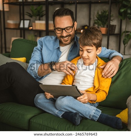 Father look son while he play video games or browse internet on tablet and enjoy at home