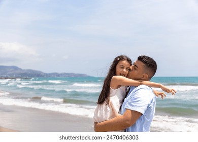 A father lovingly kisses his daughter as he holds her by the beach. The girl's face lights up with a smile, reflecting the strong bond between them. - Powered by Shutterstock