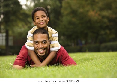 Father lying in grass smiling as son climbs on his back and hugs his neck. - Powered by Shutterstock